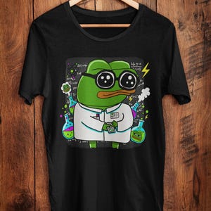 May include: Black t-shirt with a cartoon frog in glasses and a lab coat, surrounded by science graphics and equations. The frog is holding a small device. Beakers and lightning bolts are also present.