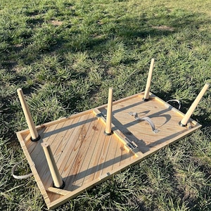 May include: A wooden folding table with a chevron pattern on the top. The table is folded up and has four legs that are attached to the underside of the table. The table is sitting on a grassy surface.