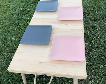 May include: A wooden folding table with a rope handle. The table has four gray and pink square plates on it.