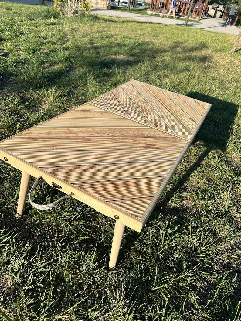 May include: A wooden folding table with a chevron pattern top and white painted legs. The table is sitting on a grassy surface.