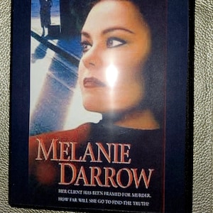 Könnte beinhalten: Ein DVD-Gehäuse mit blauem Hintergrund und dem Gesicht einer Frau auf der Vorderseite. Der Text auf dem Gehäuse lautet "DELTA BURKE" und "MELANIE DARROW". Der Text unter dem Titel lautet "HER CLIENT HAS BEEN FRAMED FOR MURDER. HOW FAR WILL SHE GO TO FIND THE TRUTH."