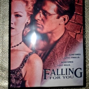 May include: A movie poster for the film "Falling for You" starring Jennie Garth, Currie Graham, Costas Mandylor, and Billy Dee Williams. The poster features a close-up of a couple, a woman with blonde hair and a man with brown hair, looking at each other. The poster has a red, white, and black colour scheme.