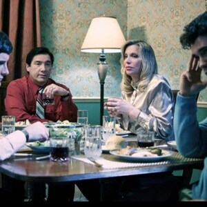 May include: A group of four people sitting around a table, eating a meal. The table is set with plates, glasses, and silverware. There is a lamp in the background.
