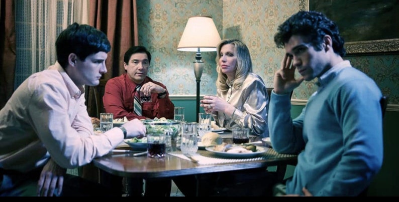 May include: A group of four people sitting around a table, eating a meal. The table is set with plates, glasses, and silverware. There is a lamp in the background.