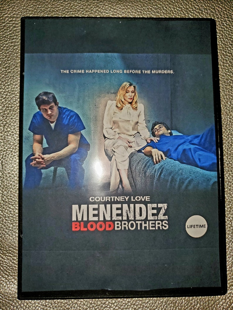 May include: DVD cover for the Lifetime movie "Menendez: Blood Brothers" starring Courtney Love. The cover features a scene from the movie with three people in a room. The text "The crime happened long before the murders." is at the top of the cover.