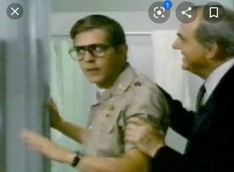 May include: A man in a khaki uniform with glasses looks nervously at another man in a dark suit. The man in the suit has his hand on the other man's shoulder.