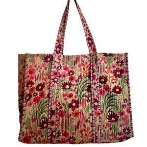 May include: A large tote bag with a floral print in shades of pink, red, green, and brown. The bag has two long straps and a quilted texture.
