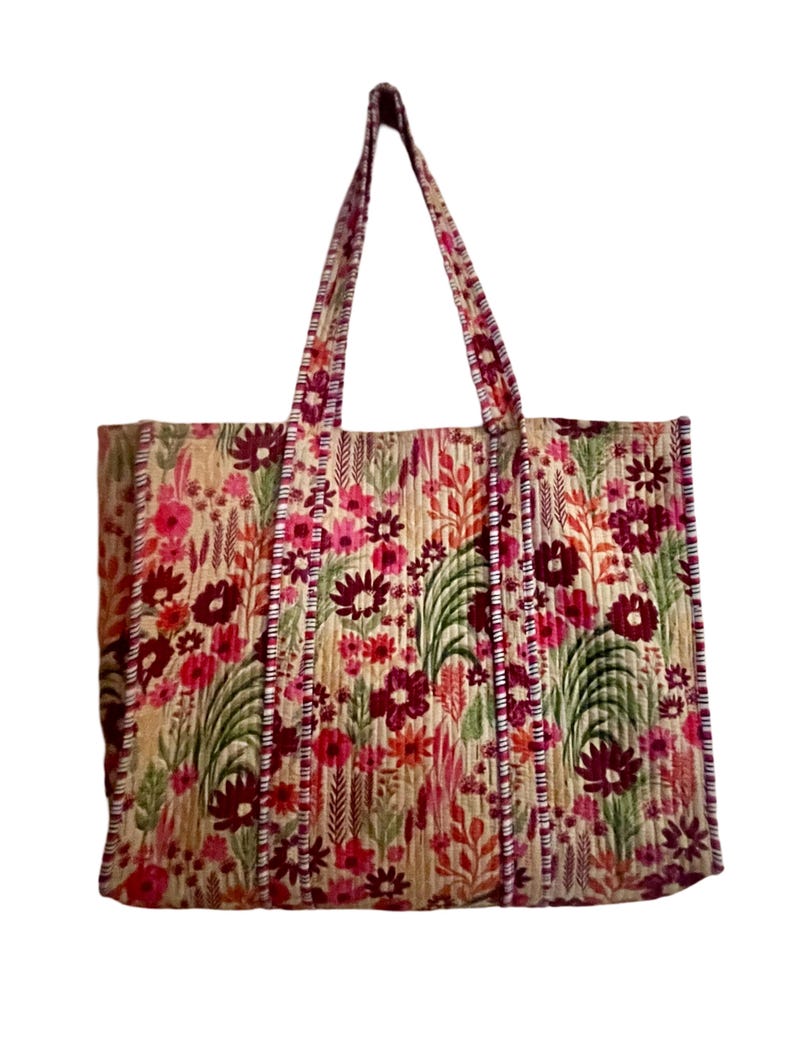 May include: A large tote bag with a floral print in shades of pink, red, green, and brown. The bag has two long straps and a quilted texture.