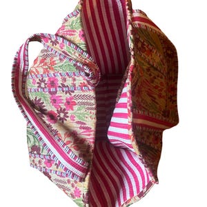 May include: A large tote bag with a floral print on the outside and a pink and white striped lining. The bag has two handles.