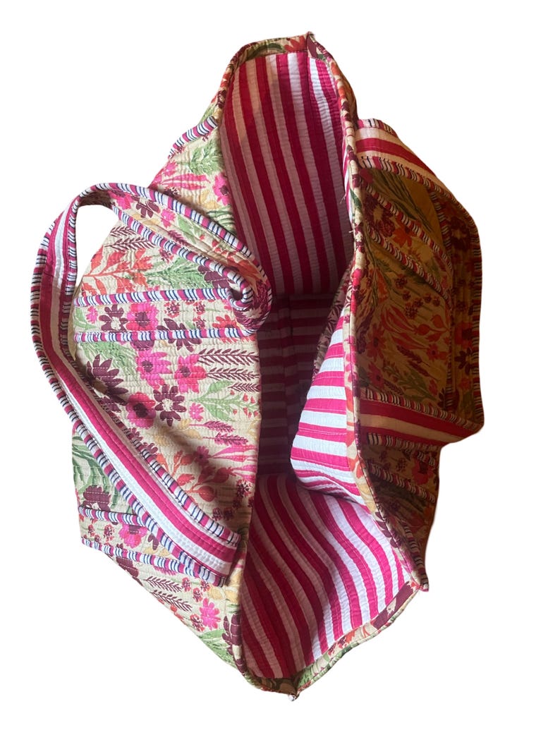 May include: A large tote bag with a floral print on the outside and a pink and white striped lining. The bag has two handles.