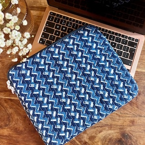 May include: A blue and white patterned laptop sleeve with a zipper closure. The sleeve is made of a quilted fabric and has a geometric design.