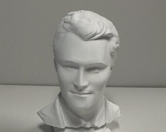 May include: A white matte bust sculpture of a person with short, styled hair, featuring a collared shirt and a square base. The name Charlie Kirk is embossed in capital letters on the front of the base, capturing the facial features in detail.