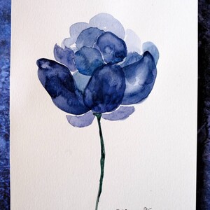 May include: Watercolor painting of a blue flower with a dark green stem. The flower has multiple layers of petals in varying shades of blue. The artist's signature, "Zhanna Vitkovska", is in the bottom right corner.