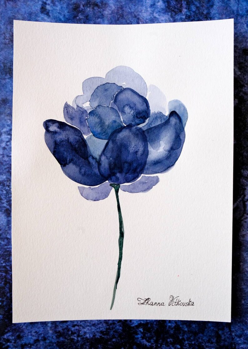 May include: Watercolor painting of a blue flower with a dark green stem. The flower has multiple layers of petals in varying shades of blue. The artist's signature, "Zhanna Vitkovska", is in the bottom right corner.
