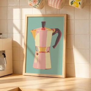 May include: A framed art print featuring a stylized illustration of a pink and yellow moka pot on a teal background. The print is displayed in a kitchen setting with a white espresso machine, a pink pleated lamp, and various ceramic mugs.