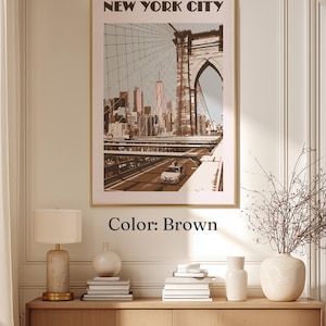 May include: A framed wall art print featuring a sepia-toned illustration of the Brooklyn Bridge and the New York City skyline. The text NEW YORK CITY is printed in bold black letters at the top. The artwork displays a car on the bridge.