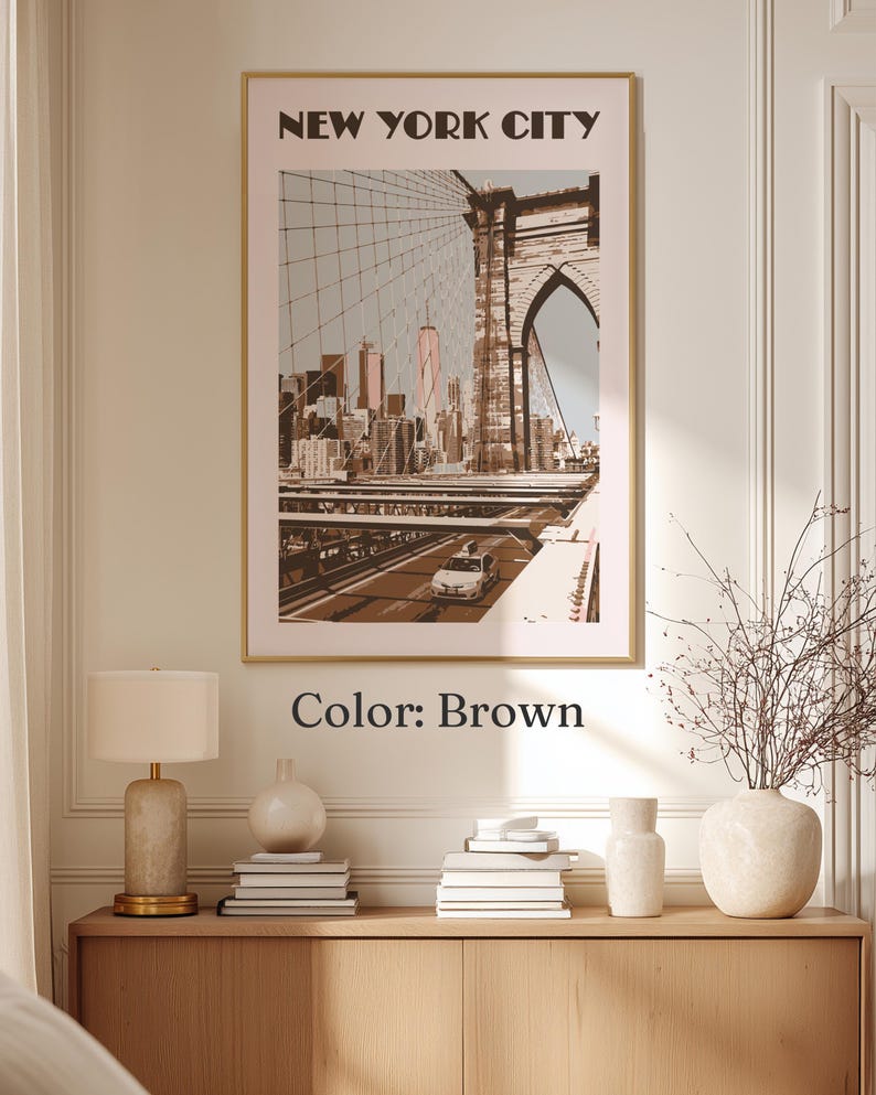 May include: A framed wall art print featuring a sepia-toned illustration of the Brooklyn Bridge and the New York City skyline. The text NEW YORK CITY is printed in bold black letters at the top. The artwork displays a car on the bridge.