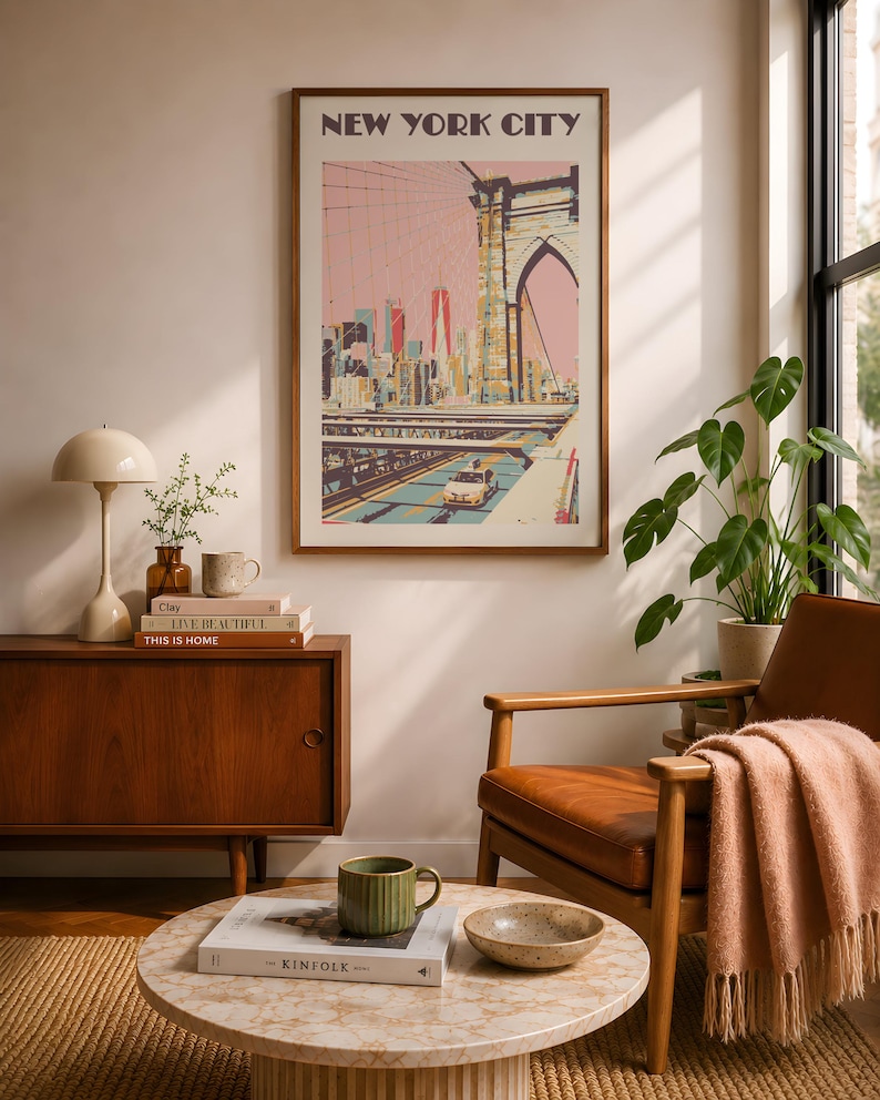 New York City travel poster displayed in a warm mid-century modern living room featuring a walnut credenza, vintage-inspired leather lounge chair, marble coffee table, natural sunlight, and indoor plants. Stylish urban apartment decor with Scandinavian influences, cozy designer styling, and a sophisticated feminine aesthetic perfect for modern home decorating and gallery wall inspiration.