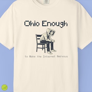 May include: A cream-colored short-sleeve t-shirt featuring a black graphic of a person sitting on a chair with a computer monitor for a head. The text reads Ohio Enough to Make the Internet Nervous in a mix of pixelated and standard fonts.