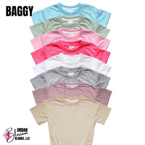 May include: A stack of eight plain, short-sleeved t-shirts in various colors, including light blue, green, pink, red, white, gray, mauve, and beige. The shirts are arranged from top to bottom in order of color. The text "BAGGY" is at the top of the image. The text "URBAN BLOSSOM BLANKS, LLC" is at the bottom of the image.