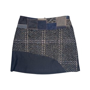 Op de afbeelding: Een patchwork minirok met een mix van stoffen en patronen. De rok combineert denim, ruitjes en textuurmaterialen in tinten blauw, grijs en neutrale tinten. Het ontwerp bevat een gebogen paneel aan de zoom.