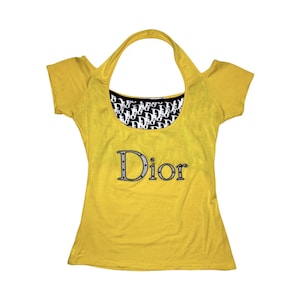 Può includere: Top giallo senape con maniche corte e la scritta "Dior" in argento e nero. Lo scollo presenta un motivo bianco e nero con il logo "Dior".