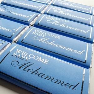 May include: A stack of blue chocolate bars wrapped in silver foil with the text "Welcome Baby Mohammed" printed in white on each bar.