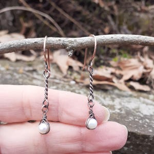 May include: A pair of copper wire earrings with a single white pearl dangling from each earring.