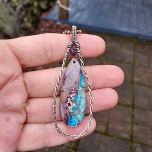 May include: A teardrop-shaped pendant with a colorful agate stone set in a copper wire frame. The pendant hangs from a copper chain.