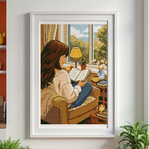 May include: A framed pixel art print depicts a person reading in a cozy room. The person is seated in a chair, holding a book, with a window view of trees and sky. A lamp, coffee cup, and flowers are on a side table.