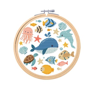 May include: A cross-stitch embroidery hoop featuring an underwater scene. The design includes a blue whale, a dolphin, various fish, starfish, a turtle, and a jellyfish. The embroidery is set in a wooden hoop.