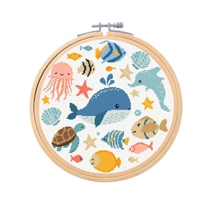 Op de afbeelding: Een borduurring met kruissteek met een onderwaterthema. Het ontwerp bevat een blauwe walvis, een dolfijn, verschillende vissen, een kwal, een zeeschildpad en zeesterren. De borduursel is in een houten ring.