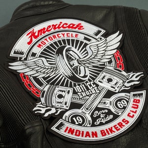 Peut inclure: Veste de moto en cuir noir avec un écusson brodé blanc et rouge qui dit "American Motorcycle 1811cc Engine Born to Ride Indian Bikers Club 1969". L'écusson représente un aigle stylisé avec les ailes déployées, un pneu et deux pistons.