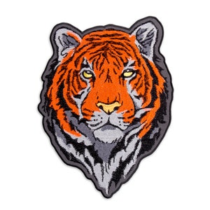 May include: Close-up of an embroidered tiger head patch with orange and black stripes, a grey muzzle, and yellow eyes.