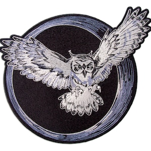 May include: A black and white embroidered patch of an owl with its wings spread, flying in a circle with a blue and white design. The owl is facing forward with its eyes open.