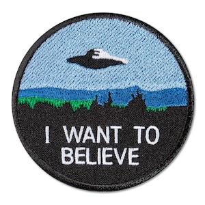 Könnte beinhalten: Ein gestickter Patch in Schwarzweiß mit einem UFO, das über einer grünen und blauen Landschaft fliegt. Der Text "I WANT TO BELIEVE" ist in Weiß unterhalb der Landschaft geschrieben.