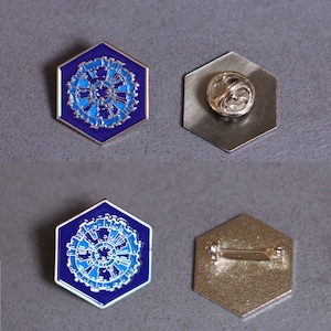 May include: A blue and silver enamel pin with a hexagonal shape. The pin features a detailed design of a circular object with a blue center and silver outer ring. The back of the pin is silver and has a safety pin closure.