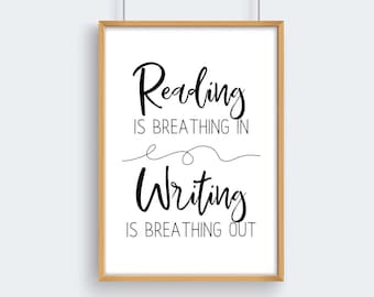 May include: A rectangular wall art print in a light wood frame featuring black text on a white background that reads: Reading IS BREATHING IN, a decorative line, Writing IS BREATHING OUT. The design uses a mix of script and sans-serif fonts.