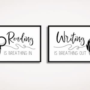May include: Two black framed prints with white backgrounds. The left print features a magnifying glass and the text "Reading is breathing in". The right print features a feather and the text "Writing is breathing out".