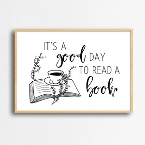 May include: A rectangular wall art print in a light wood frame featuring the black text IT'S A good DAY TO READ A book. The illustration includes an open book with a teacup resting on its pages, accented by delicate black line-drawn vines.