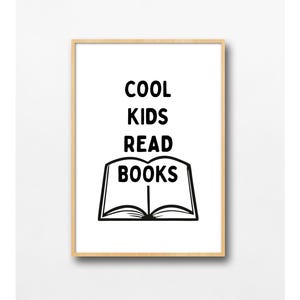 May include: A rectangular wall art print in a light wood frame featuring a white background with black text that reads COOL KIDS READ BOOKS above a simple black line drawing of an open book. The design is centered within the frame.