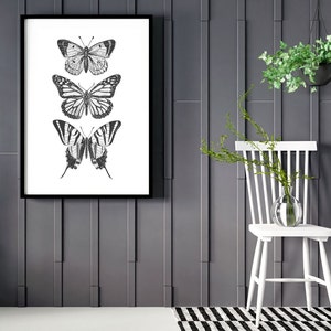 May include: A black and white framed print of three butterflies on a white background. The butterflies are arranged vertically, with the largest butterfly at the bottom and the smallest butterfly at the top. The print is hanging on a gray wall.
