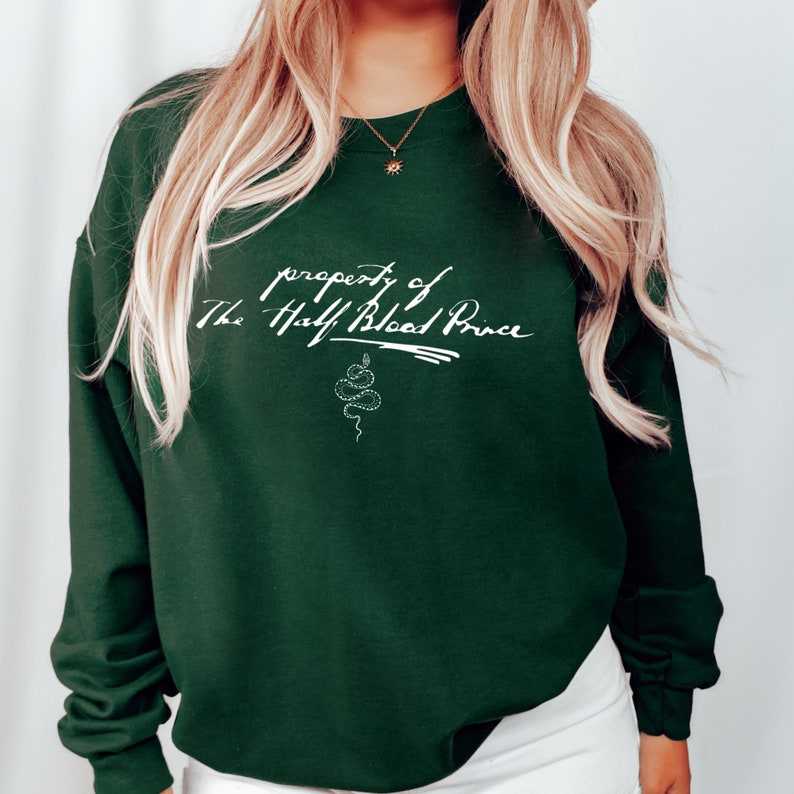 May include: A dark green sweatshirt with the text "property of The Half-Blood Prince" in white cursive lettering and a white snake illustration.