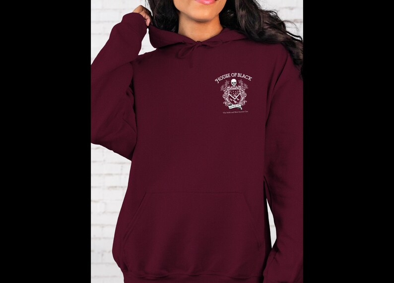 May include: A maroon hoodie with a front pocket and a hood. The upper left chest area features a white graphic with the words "HOUSE OF BLACK" and other text. The hoodie is made of a soft material.