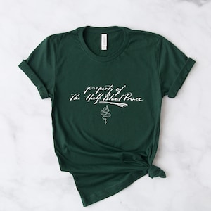 May include: A dark green t-shirt with the text "property of The Half-Blood Prince" in white cursive writing and a white snake illustration.