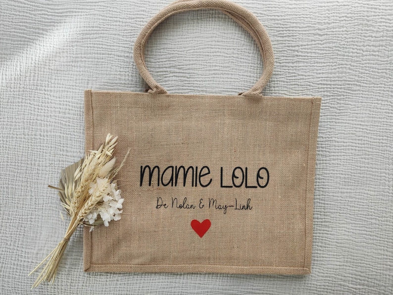 May include: A brown burlap tote bag with black embroidered text that reads "Mamie Lolo De Nolan & May-Linh" and a red heart.