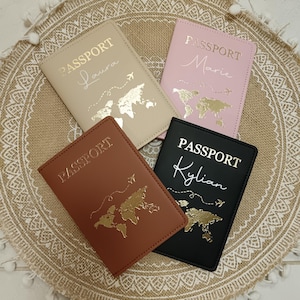 Peut inclure: Quatre étuis de passeport beiges, roses, marron et noirs. Chacun porte l'inscription "PASSPORT" en argent, un motif de carte du monde et un nom : Laura, Marie, Kylian. Les étuis sont sur un tapis décoratif beige.