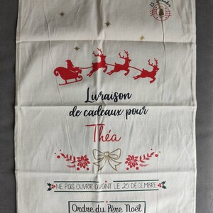 May include: Cream Christmas gift bag with red and gold details. Depicts Santa and reindeer, with text saying "Delivery of gifts for Thea" and "Do not open before December 25th". Includes a drawstring closure for securing gifts.