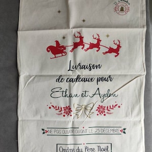 May include: A cream-coloured Christmas gift bag featuring a red Santa and reindeer design. The bag has French text: "Delivery of gifts for Ethan and Ayden" and "Do not open before December 25th."