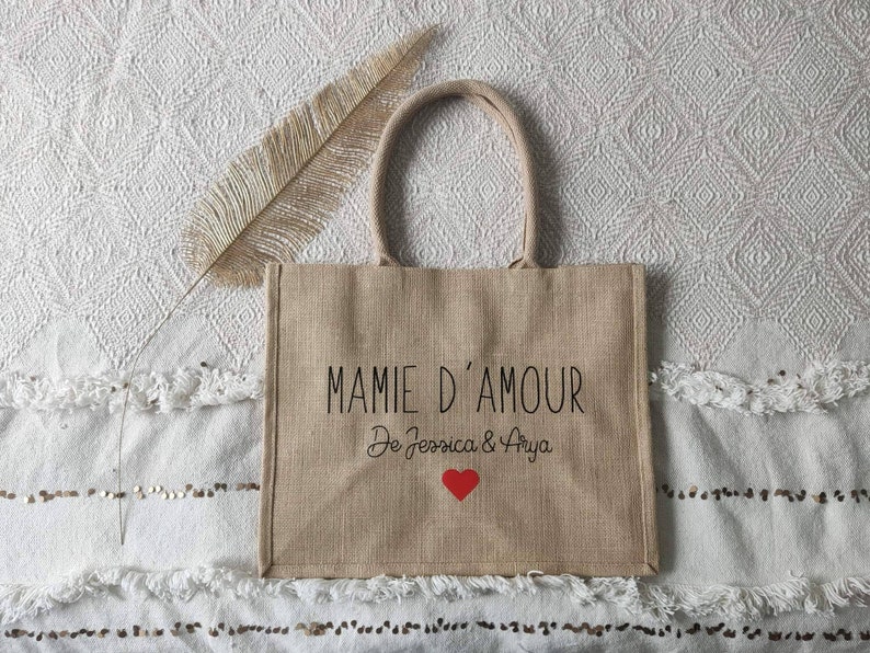 May include: A brown burlap tote bag with black text that reads "Mamie d'Amour De Jessica & Arya" with a red heart.